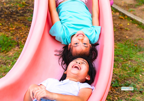 Two kids telling jokes in summer on a slide